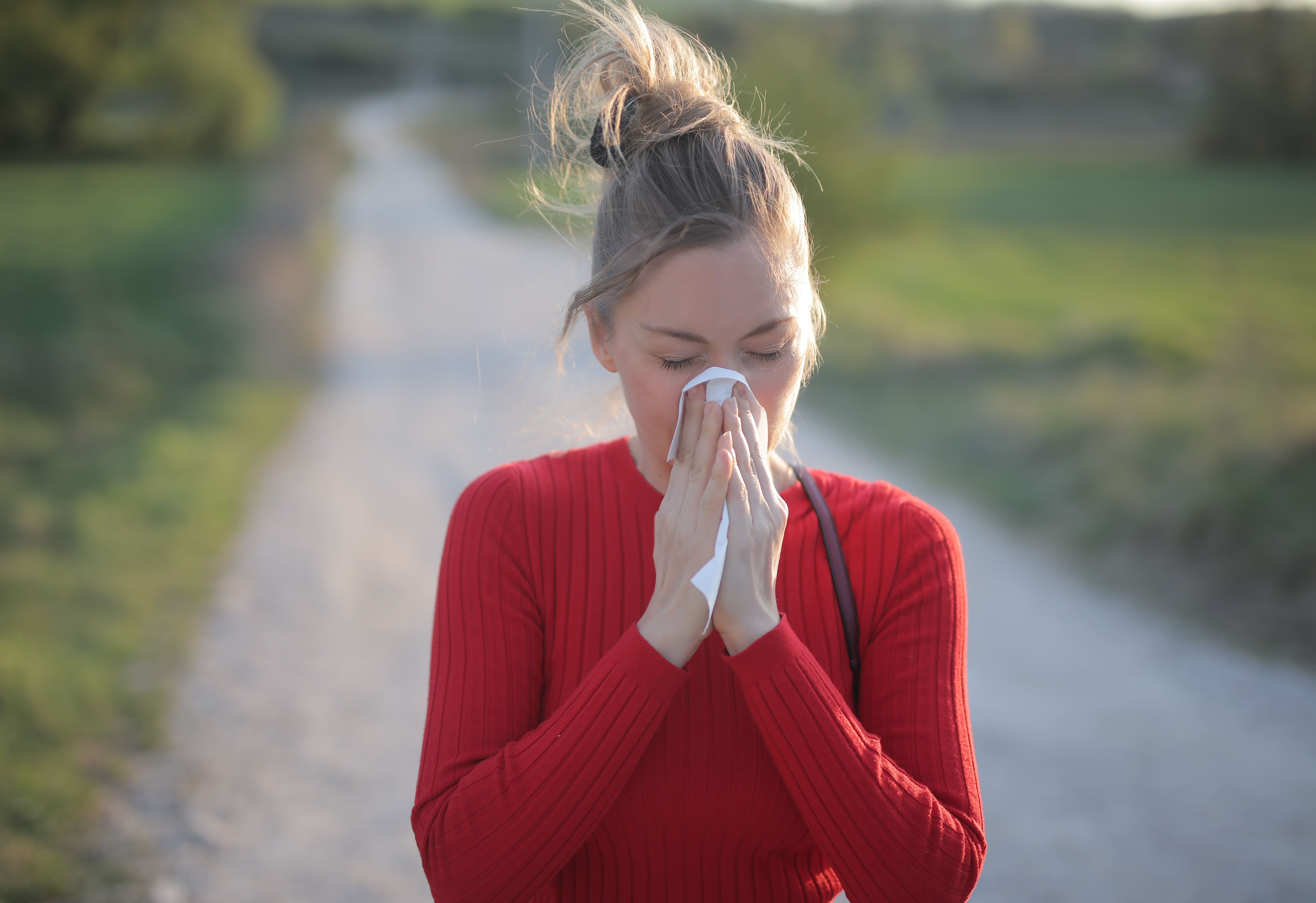 En extérieur, une femme au pull rouge se mouche