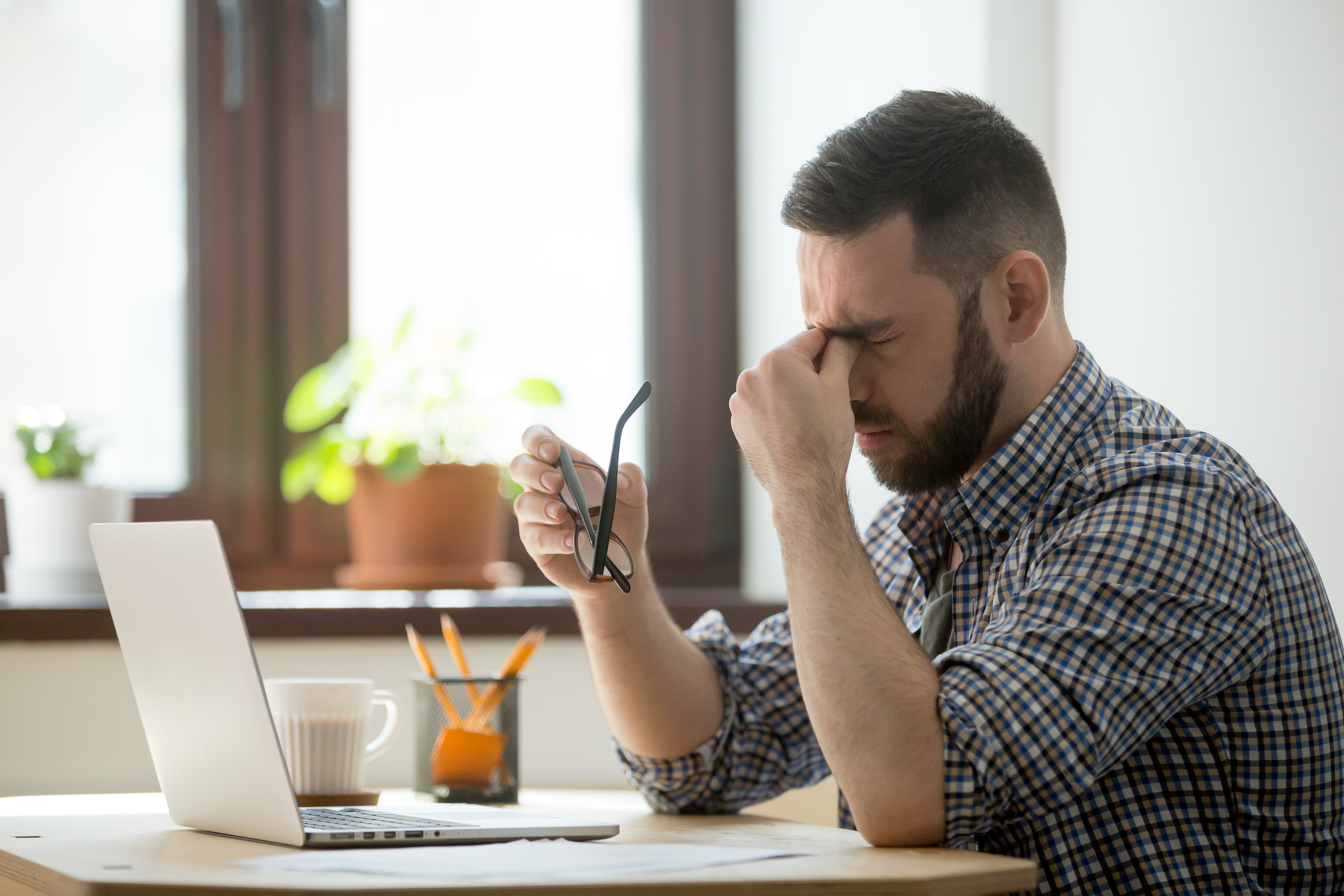 Un homme fatigué se tient le nez et a ses lunettes dans la main