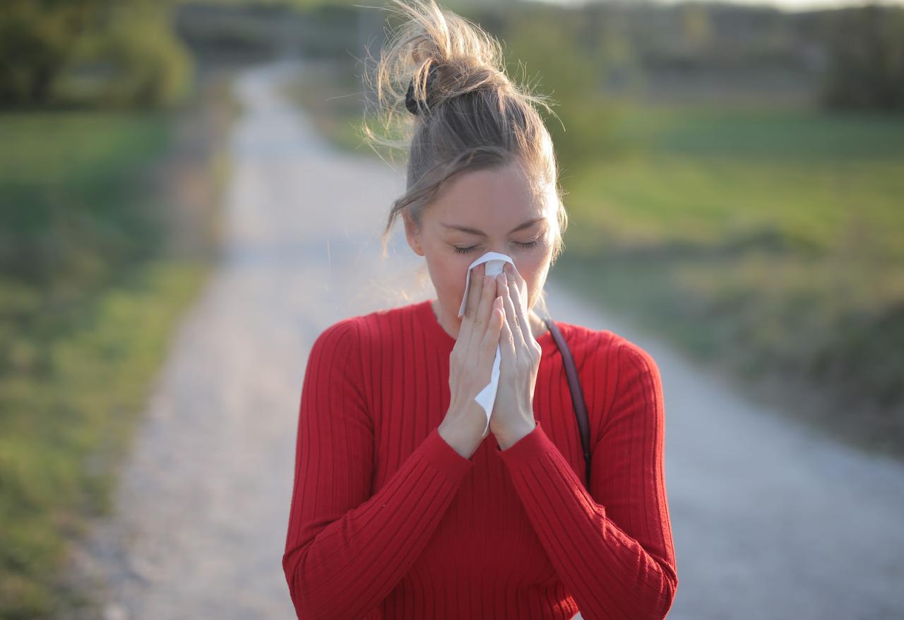 En extérieur, une femme au pull rouge se mouche