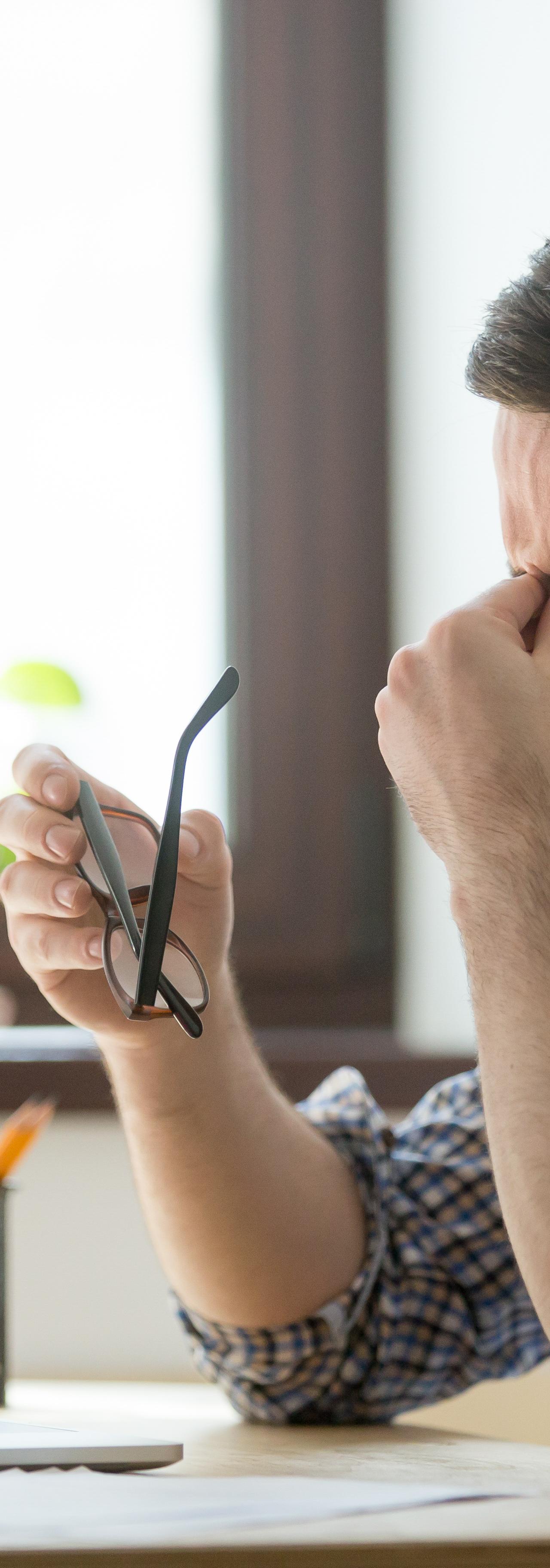 Un homme fatigué se tient le nez et a ses lunettes dans la main